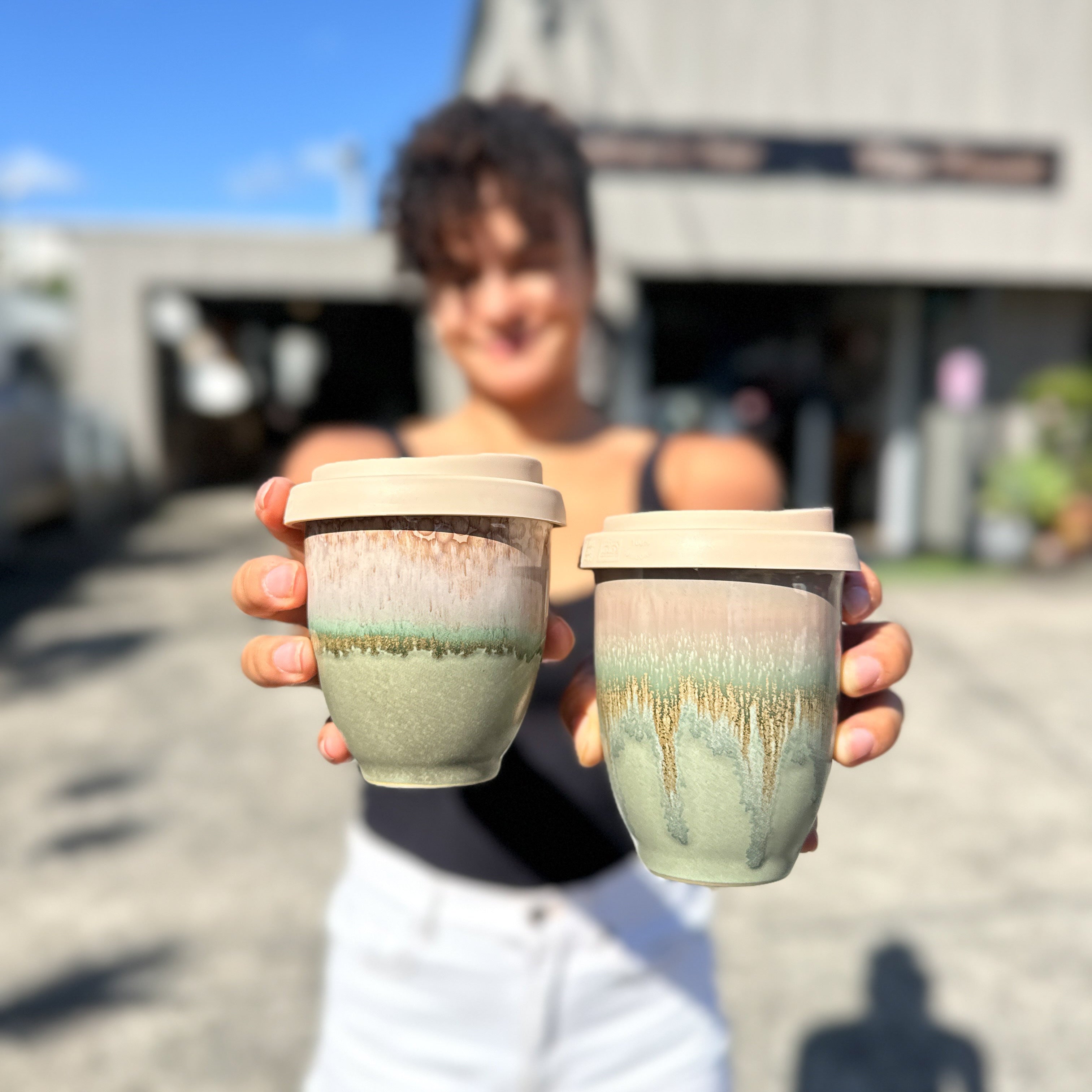 Person holding two ceramic cups outdoors with a blurred background