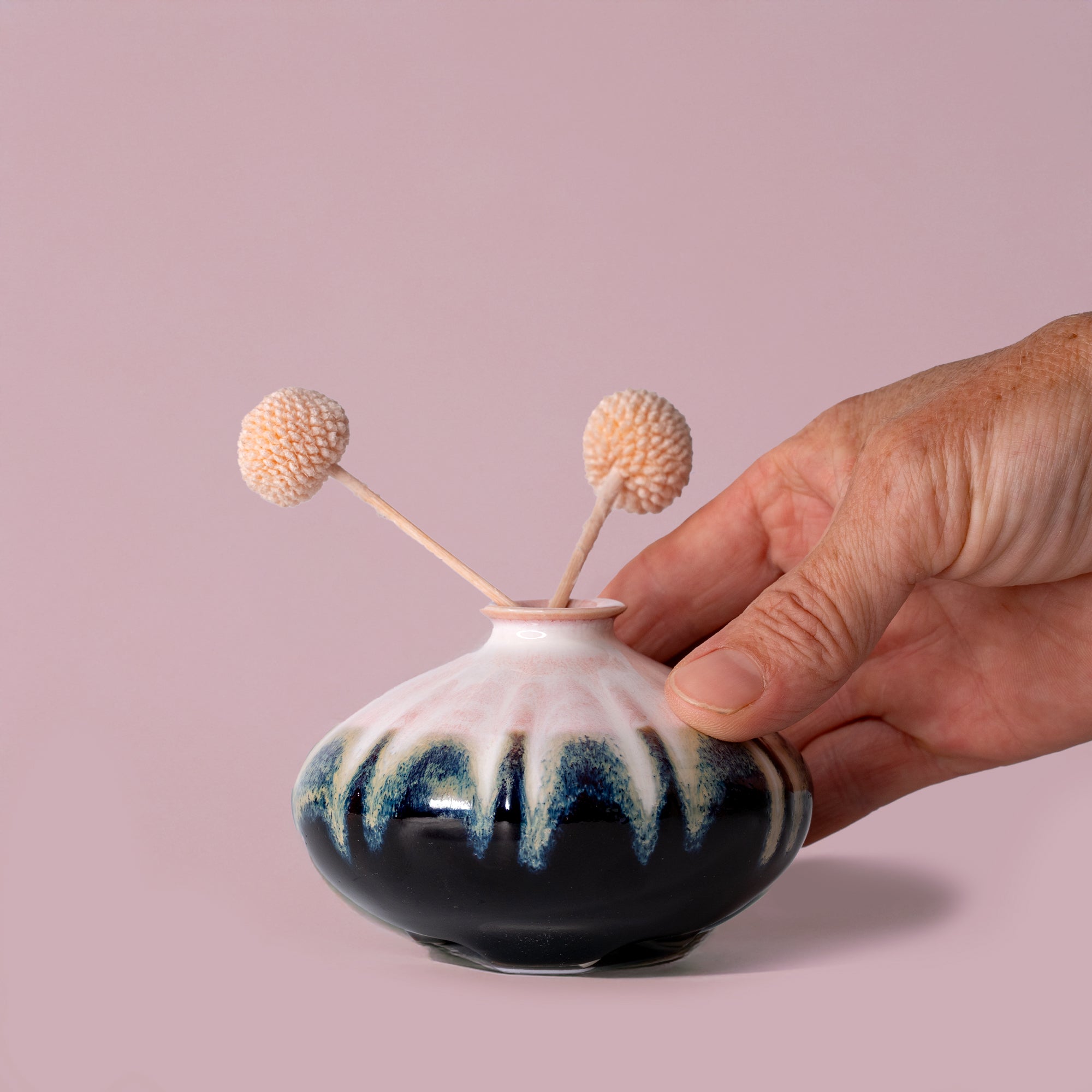 Hand holding a small black and white ceramic artisan decorative vase with two dried flowers