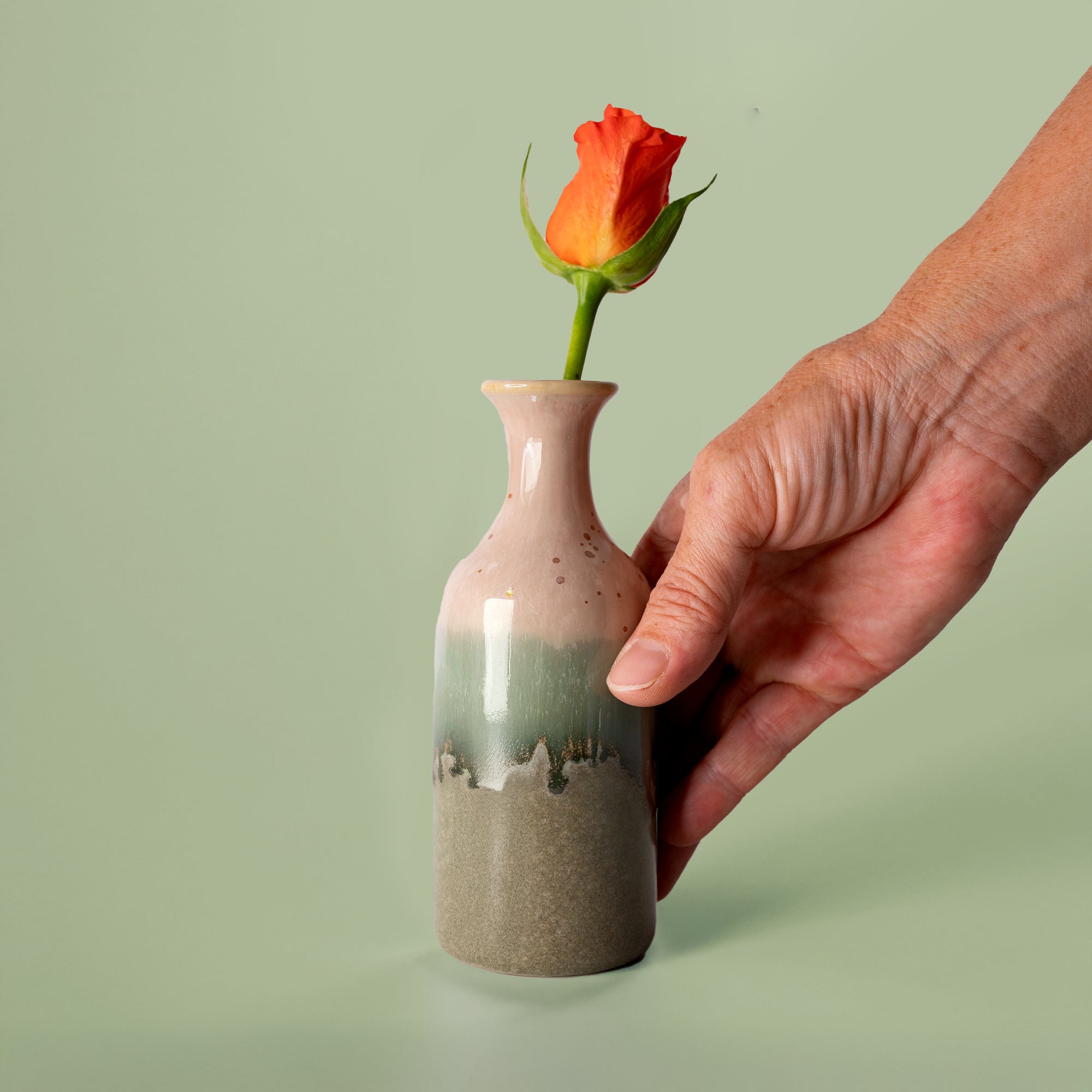 Pottery For The Planet small handmade flower vase with green and pink glaze holding an orange rose