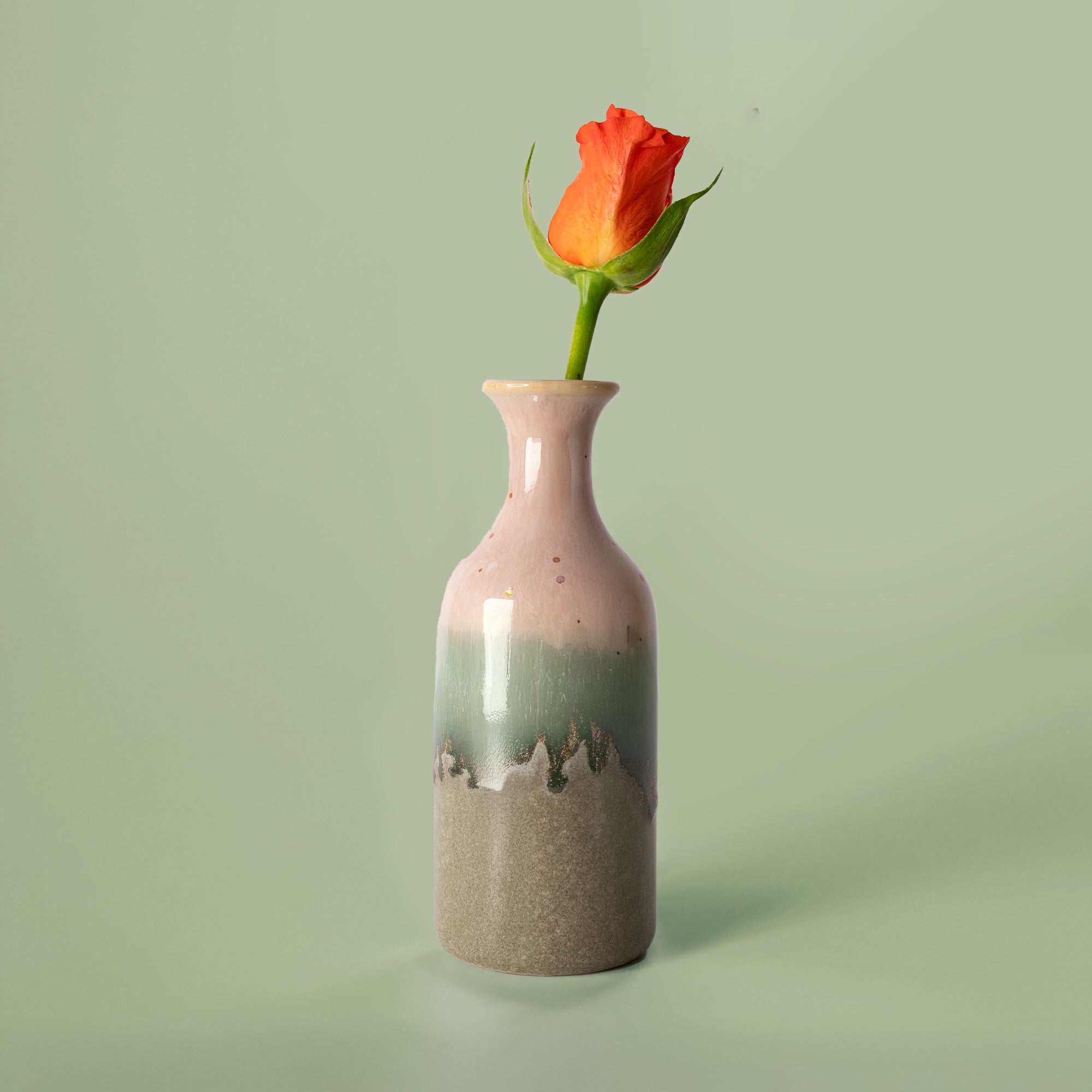Small handmade flower vase by Pottery For The Planet with pink green and brown glaze holding an orange rose