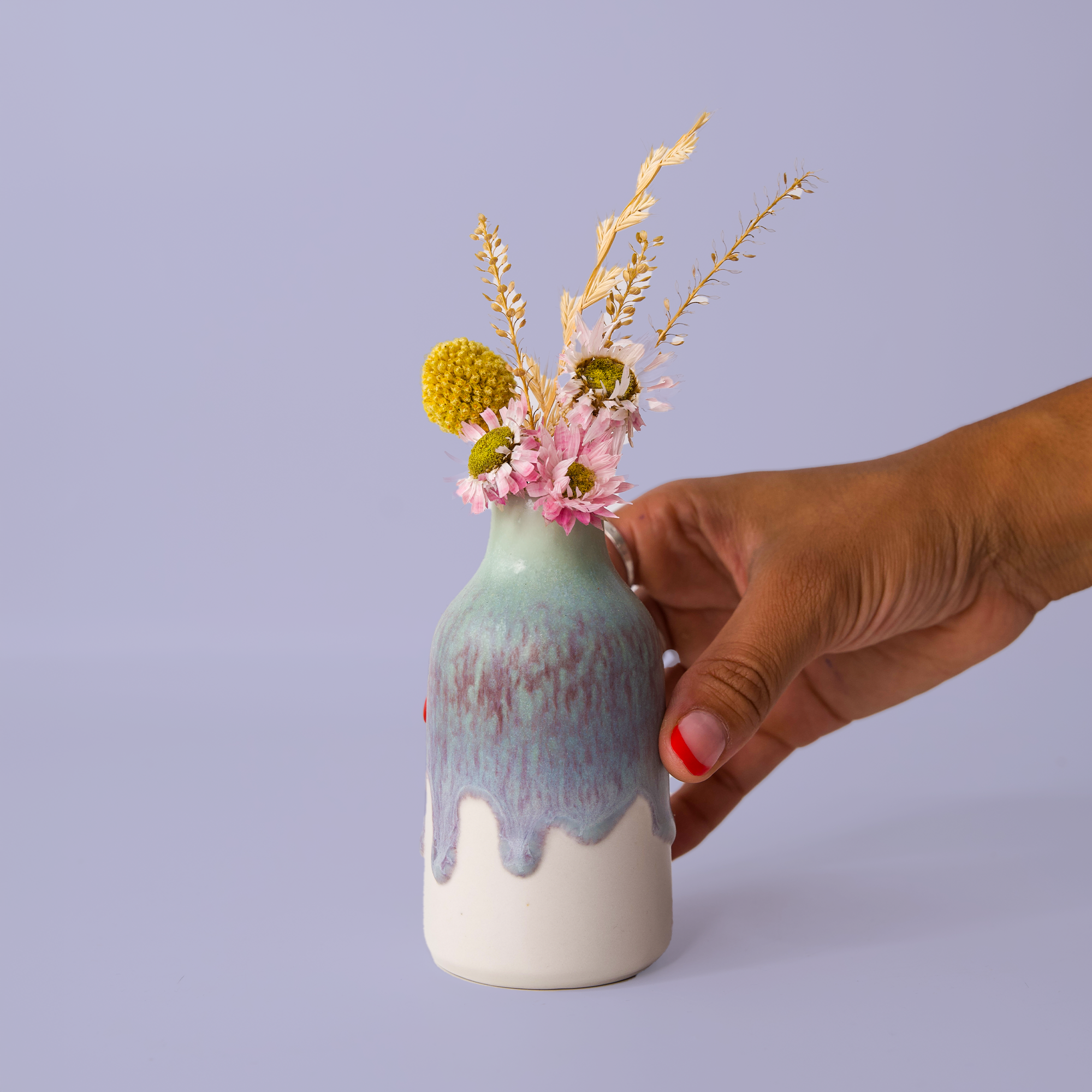 Hand holding a modern decorative flower vase by Pottery For The Planet with dried flowers on a light background
