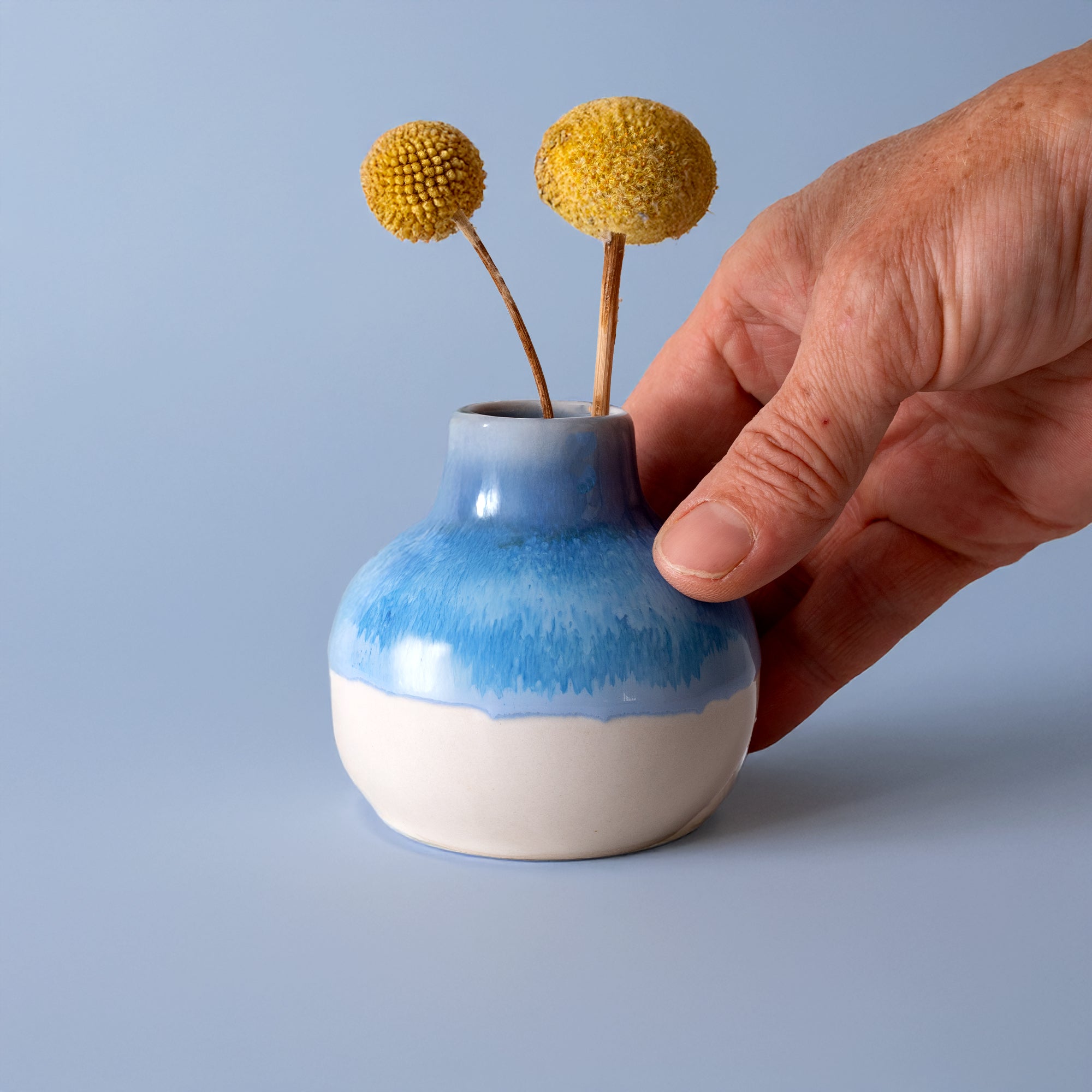 Small handmade home decor vase in blue and white ceramic held by a hand with yellow flowers
