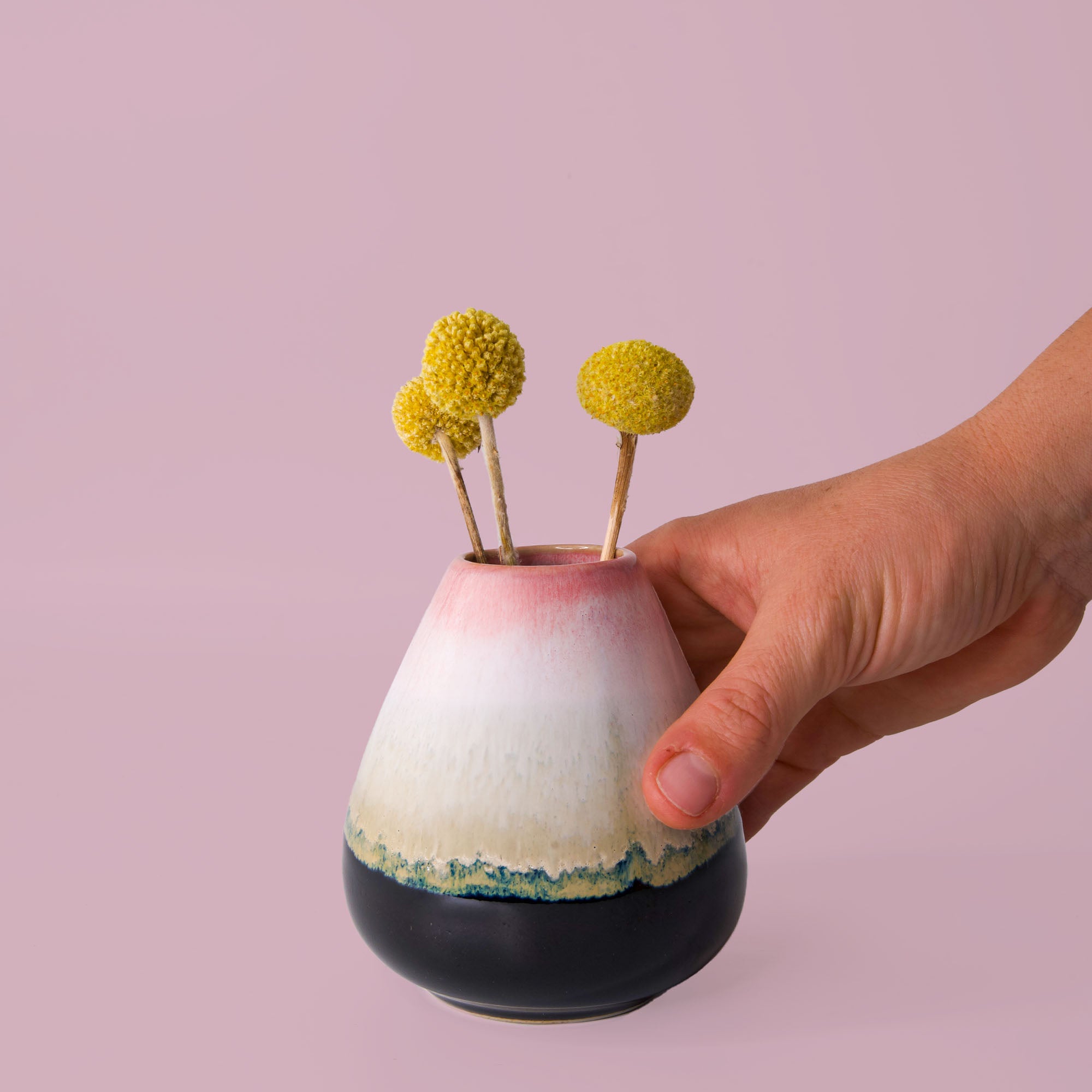 Hand holding a unique pottery flower vase in pink white and black with yellow flowers on pink background