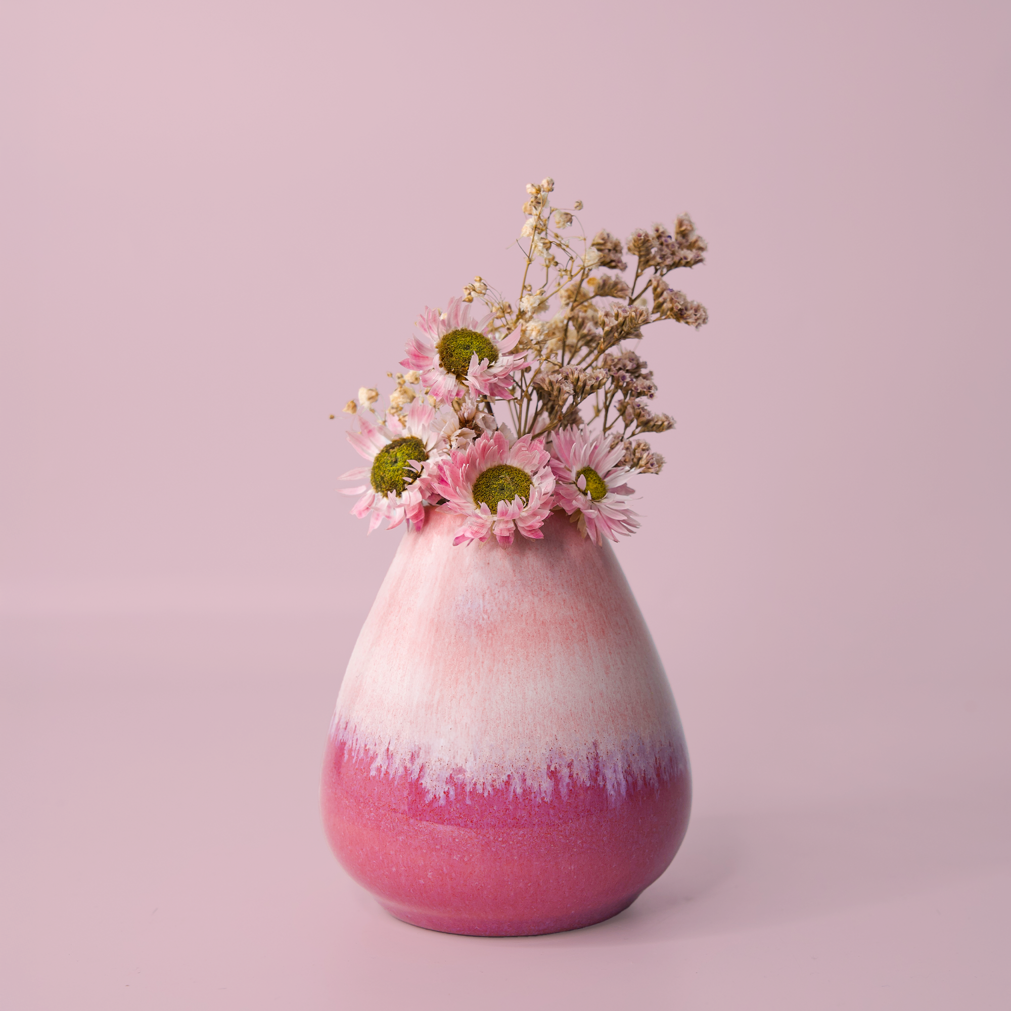 Pink and white unique pottery flower vase with dried and fresh flowers on pink background