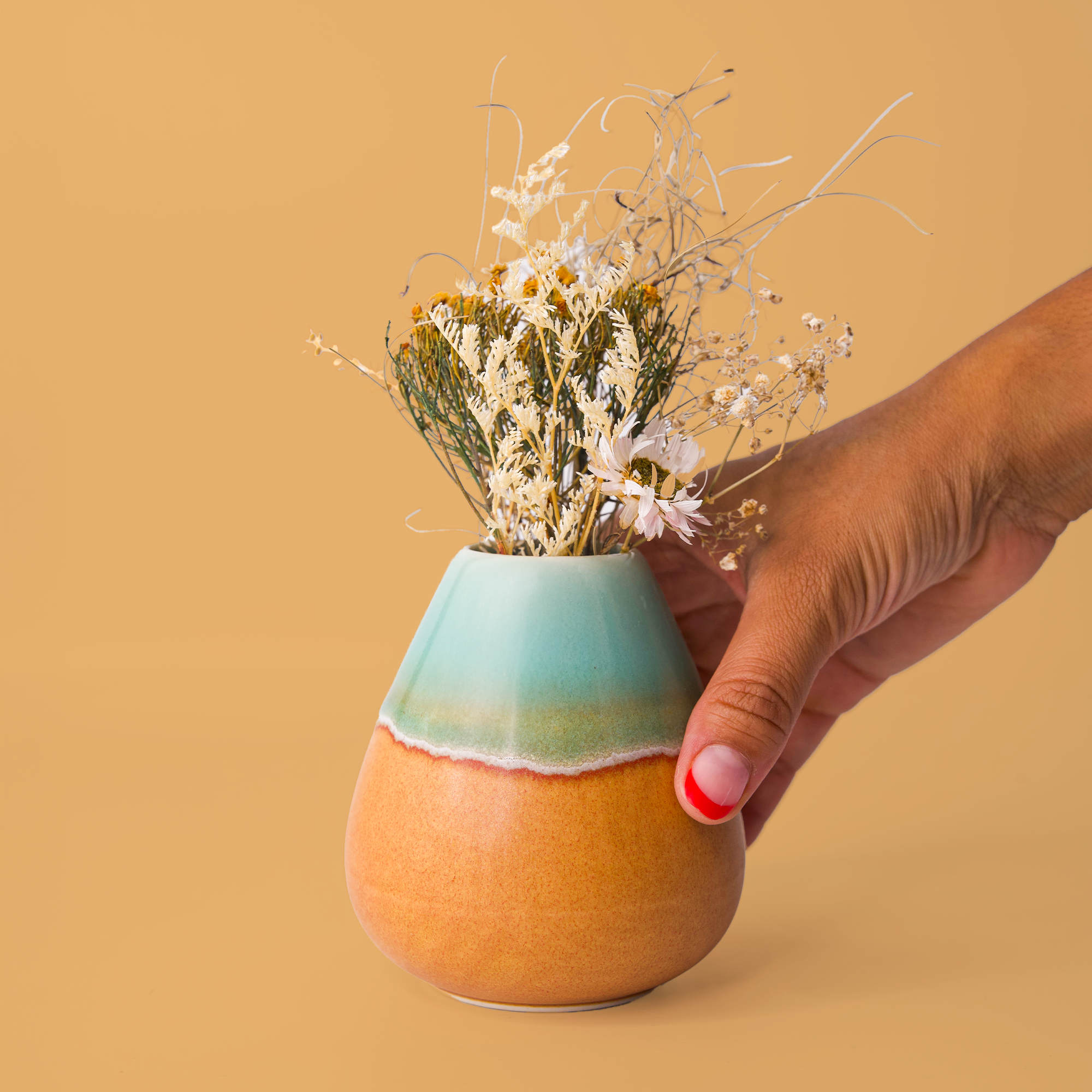 Hand holding unique pottery flower vase with blue and orange glaze filled with dried wildflowers