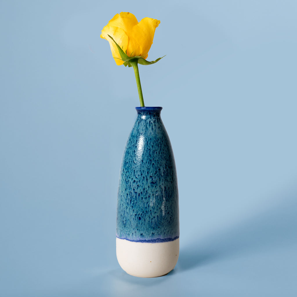 Blue and white artisan decorative vase for flowers holding a single yellow rose on blue background
