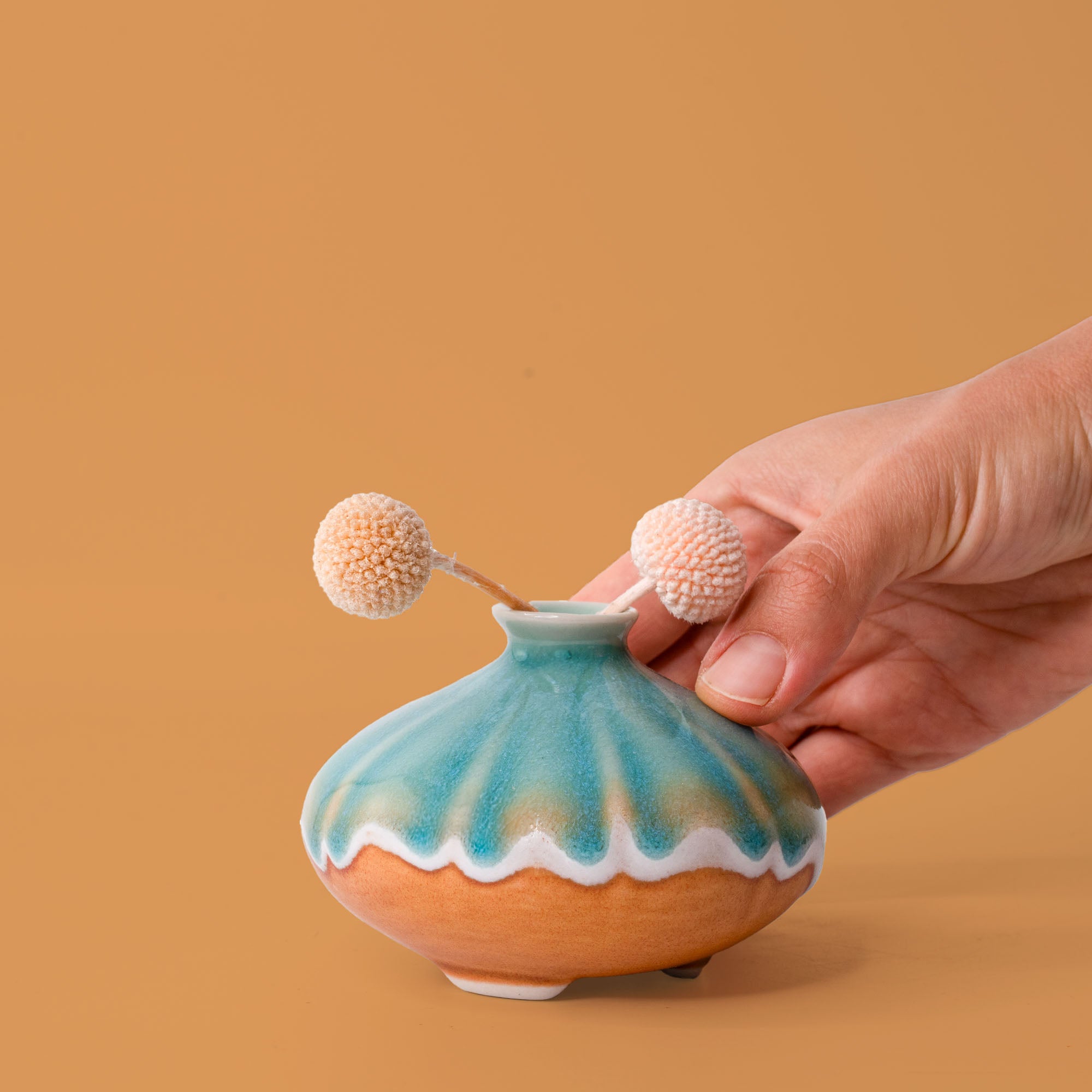 Hand holding a small blue and brown artisan decorative vase with dried flowers