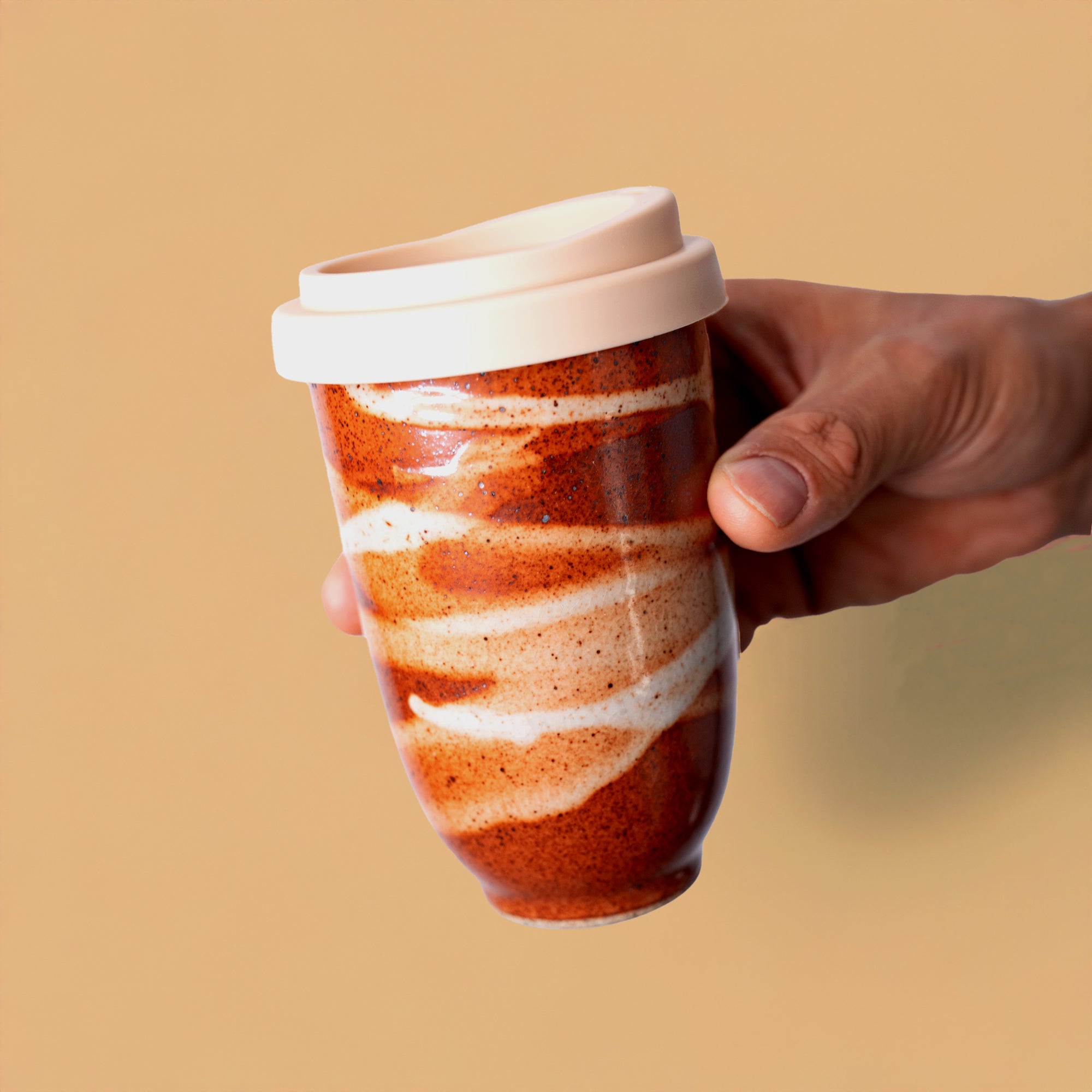 Hand holding artisan pottery travel cup with red and white swirls and a white lid
