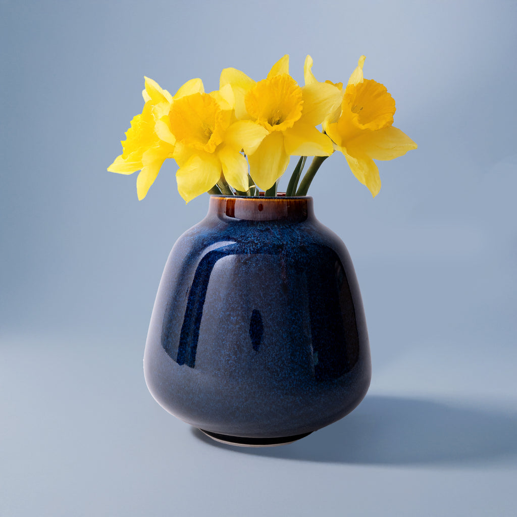 Blue ceramic bouquet vase for home decor with bright yellow daffodils on a blue background