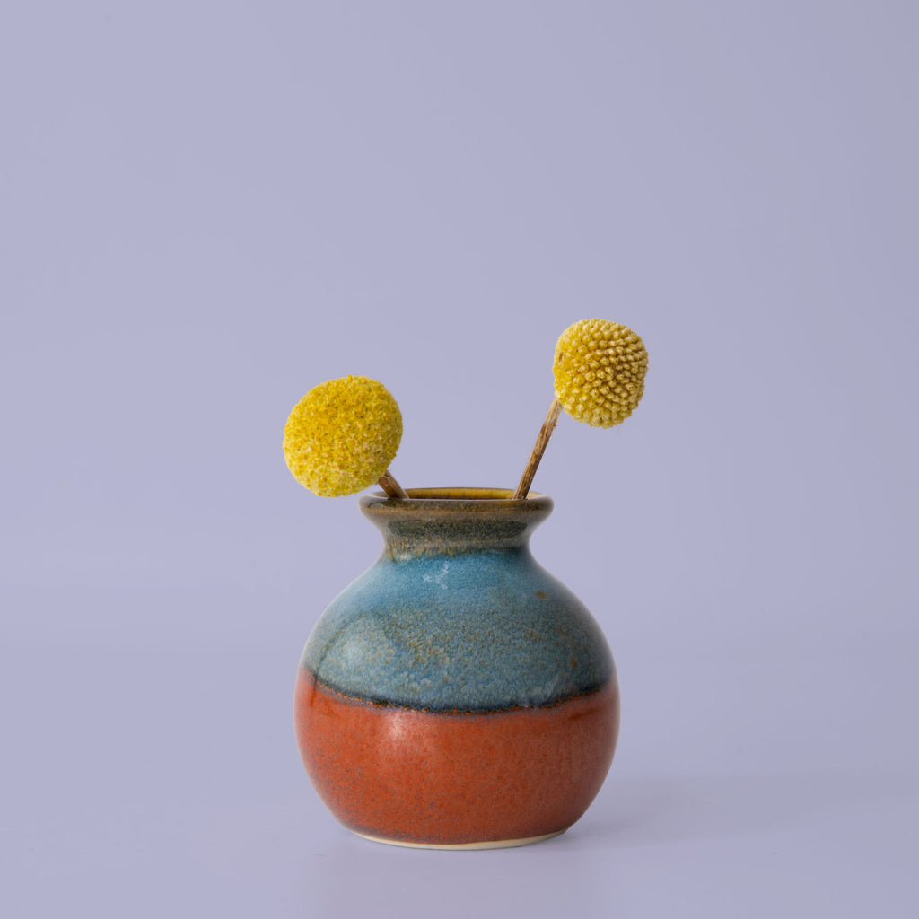 Pottery For The Planet eco-friendly home decor vase with blue and orange glaze holding two yellow billy ball flowers