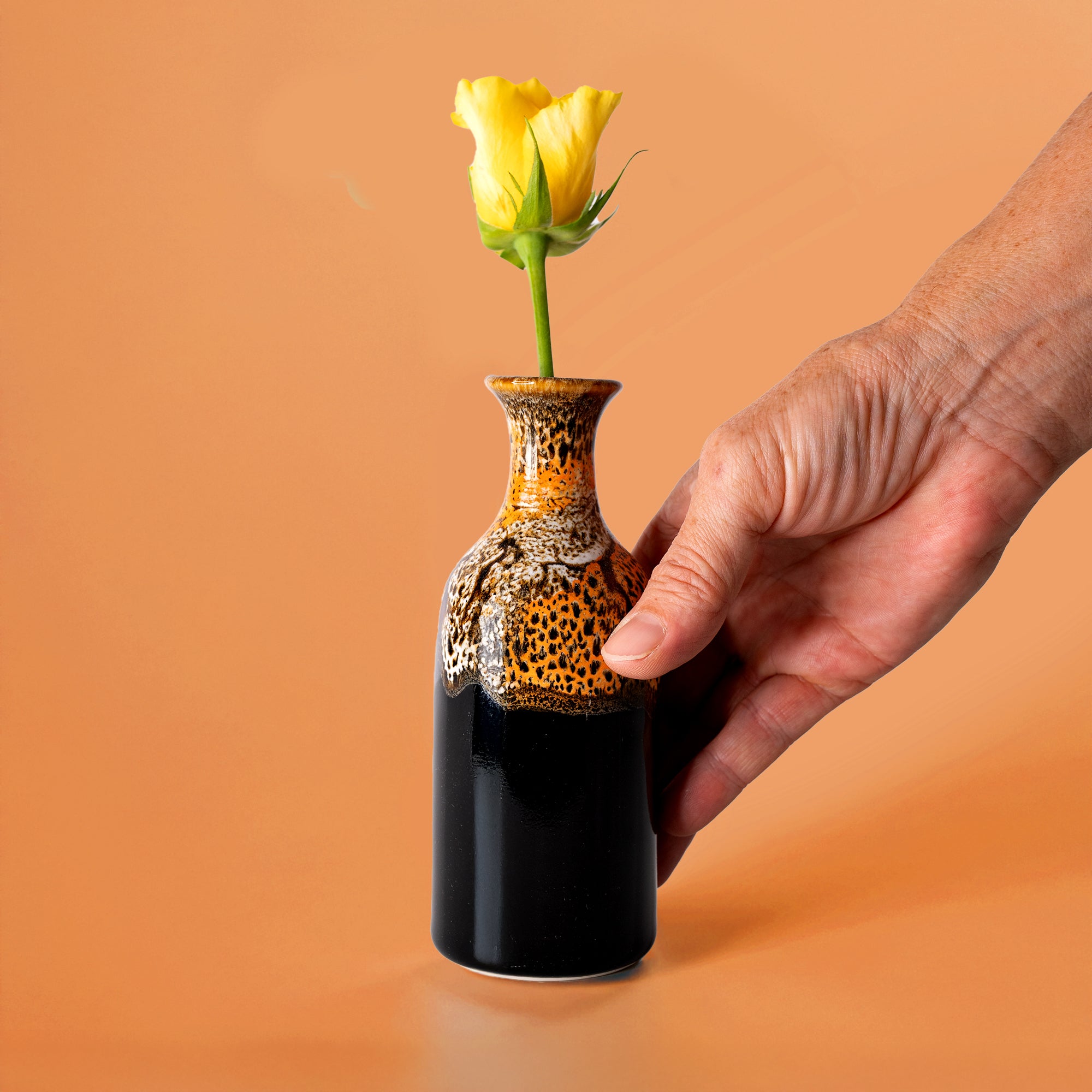 Pottery For The Planet small handmade flower vase in black and brown held with a yellow flower inside