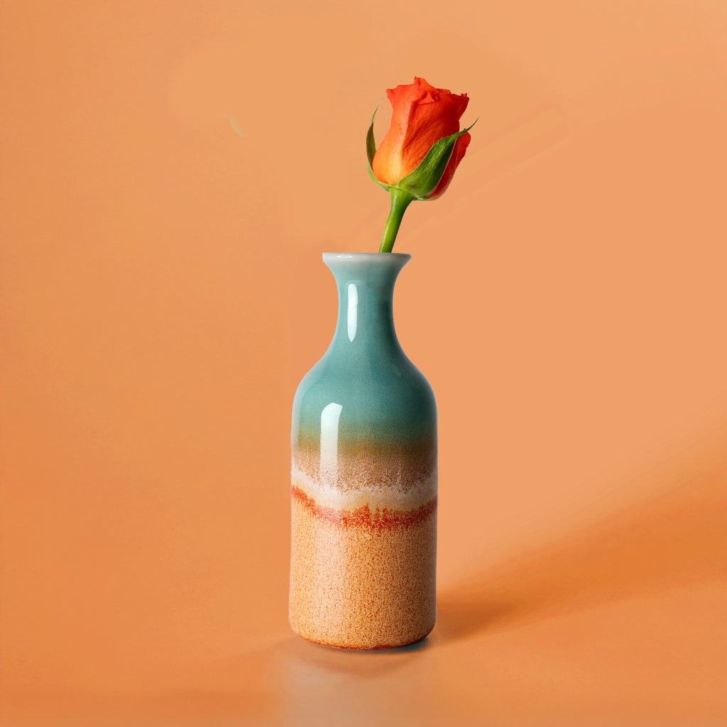 Small handmade flower vase with blue and beige gradient glaze holding a single orange rose