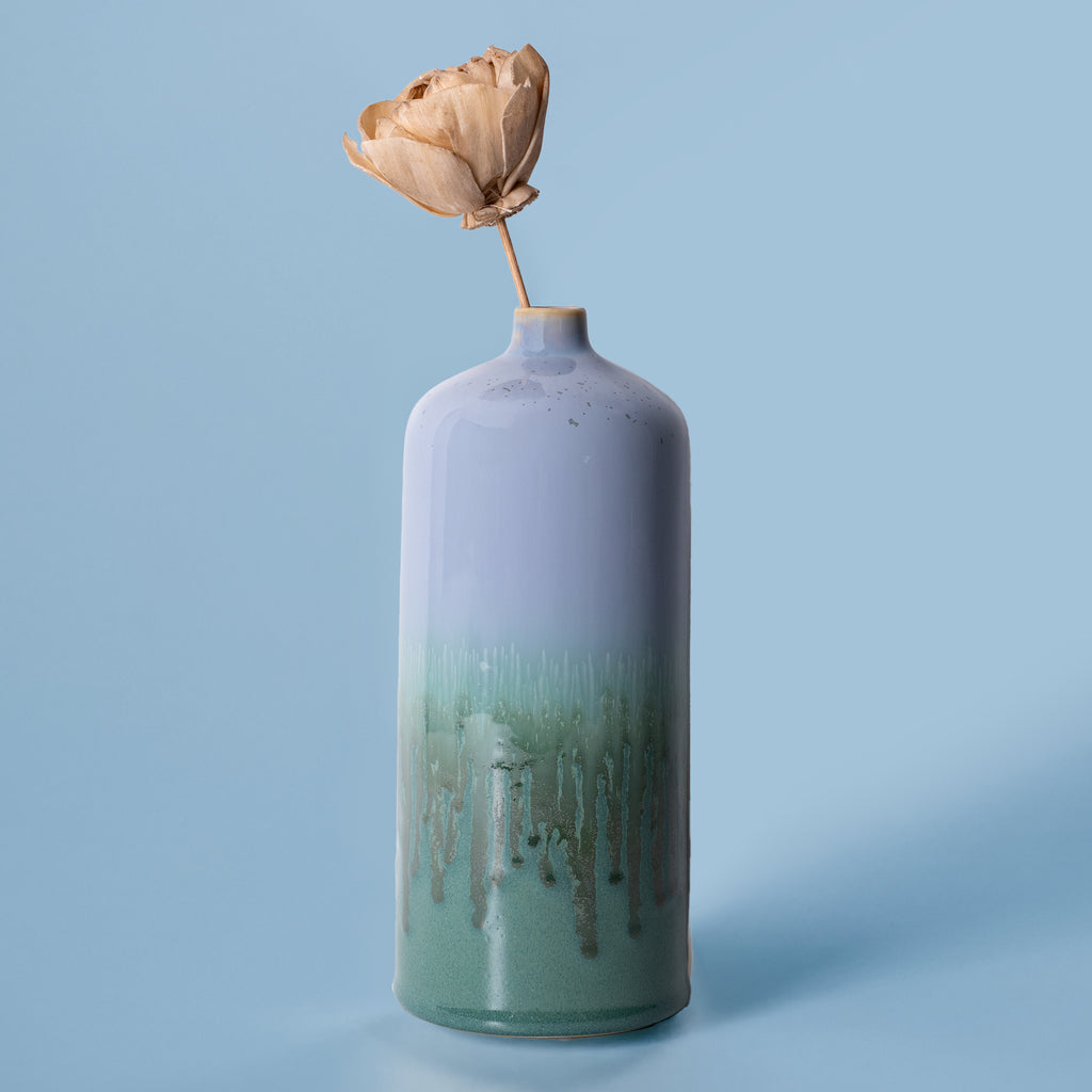 Pottery For The Planet medium decorative bud vase in blue and green with a dried flower on a light blue background