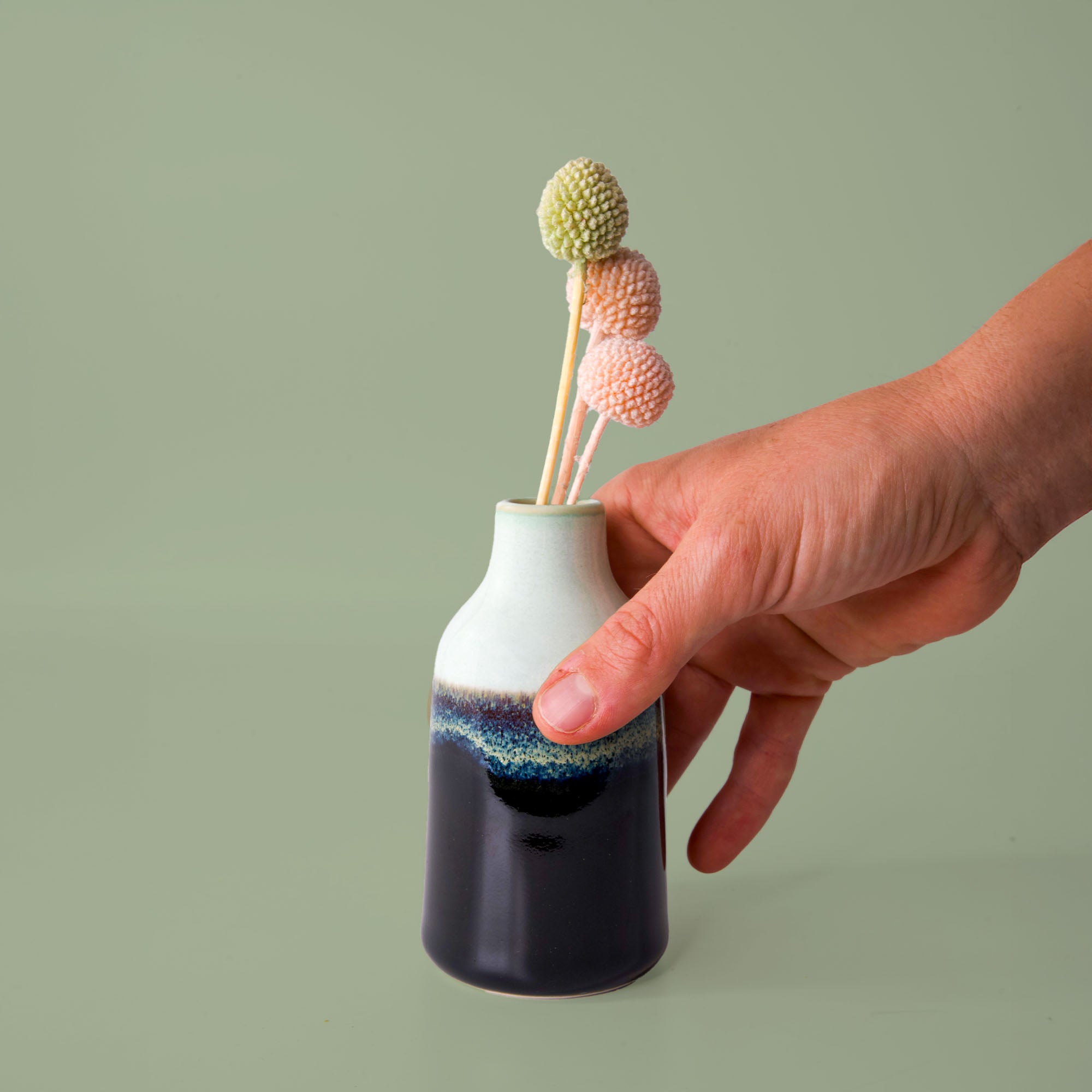 Hand holding a modern decorative flower vase with textured black and white glaze and pastel dried flowers