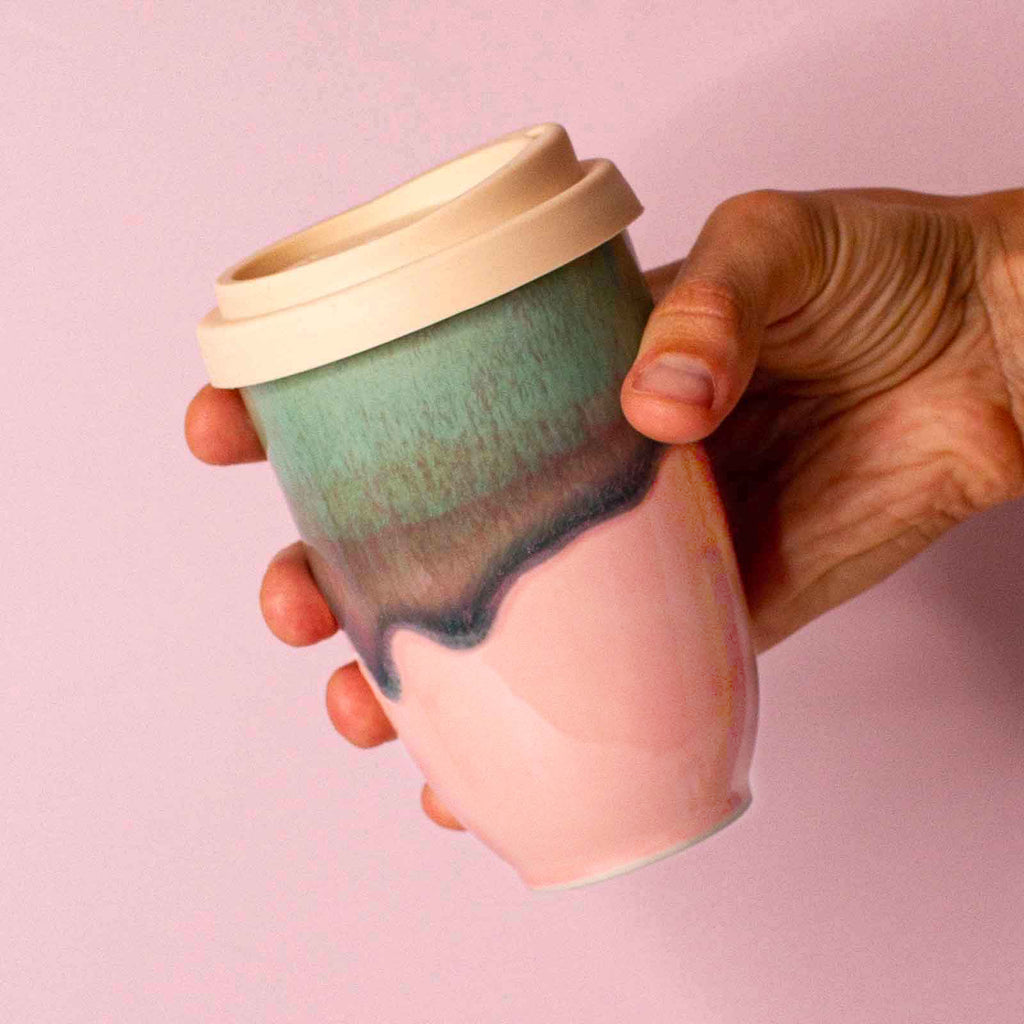 Hand holding pink ceramic travel cup with green and beige gradient and a beige lid