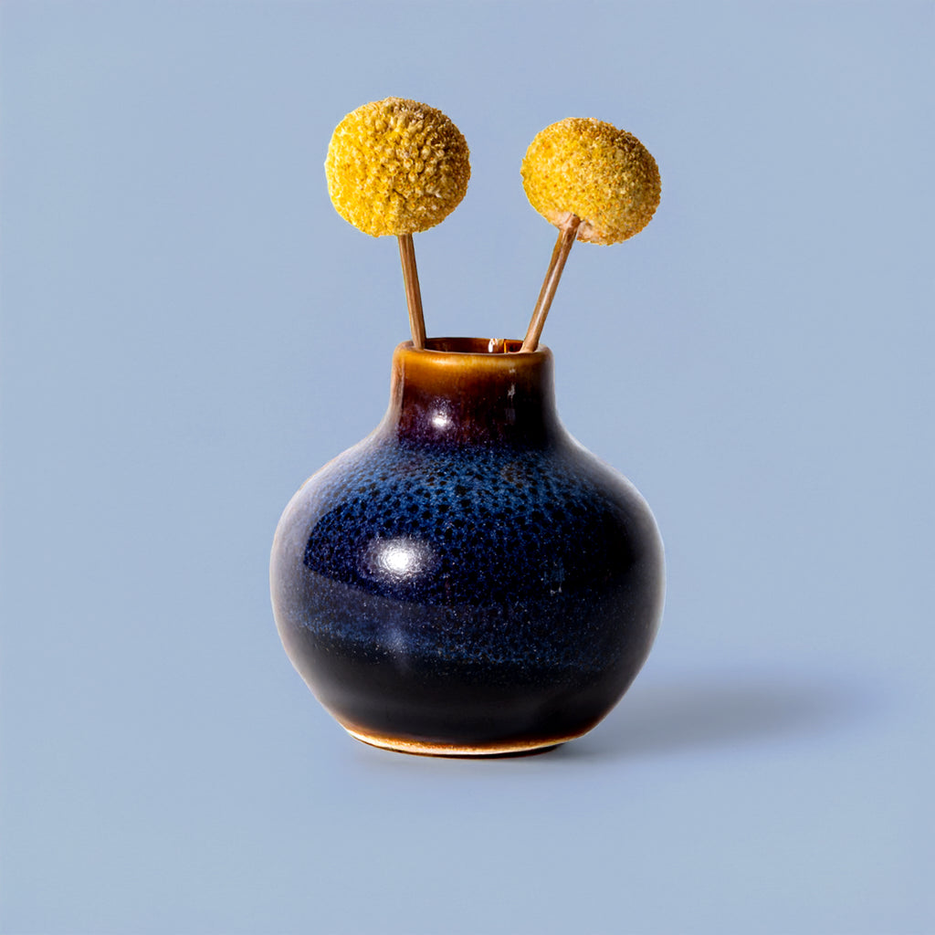 Small handmade home decor vase by Pottery For The Planet with a blue and brown glaze holding yellow billy ball flowers