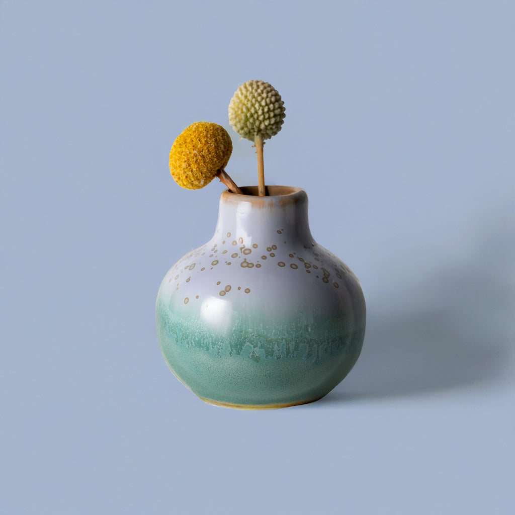 Small handmade home decor vase with green and white glaze and gold speckles holding two billy ball flowers