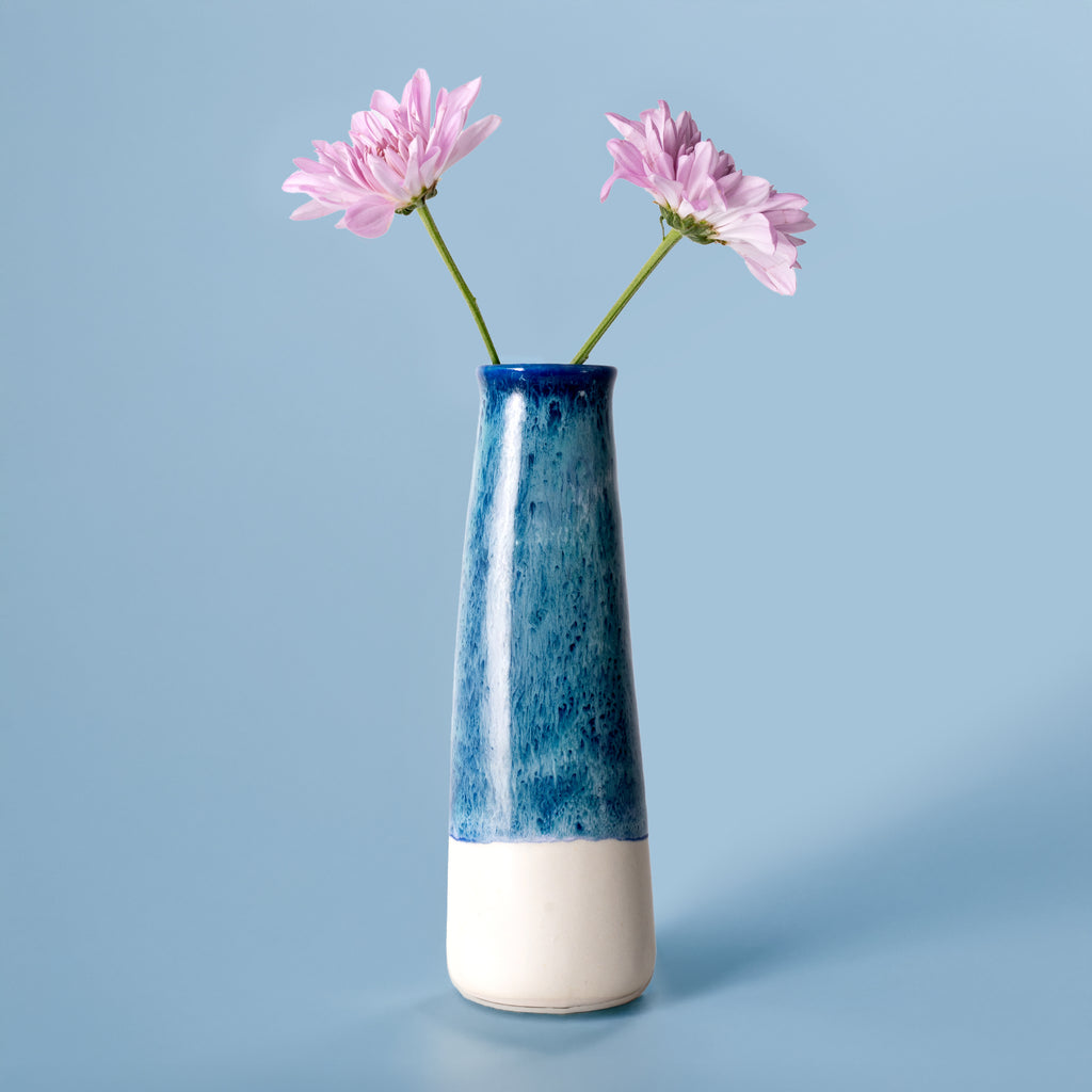 Two-toned blue and white sustainable home decor vase by Pottery For The Planet with pink flowers on blue background