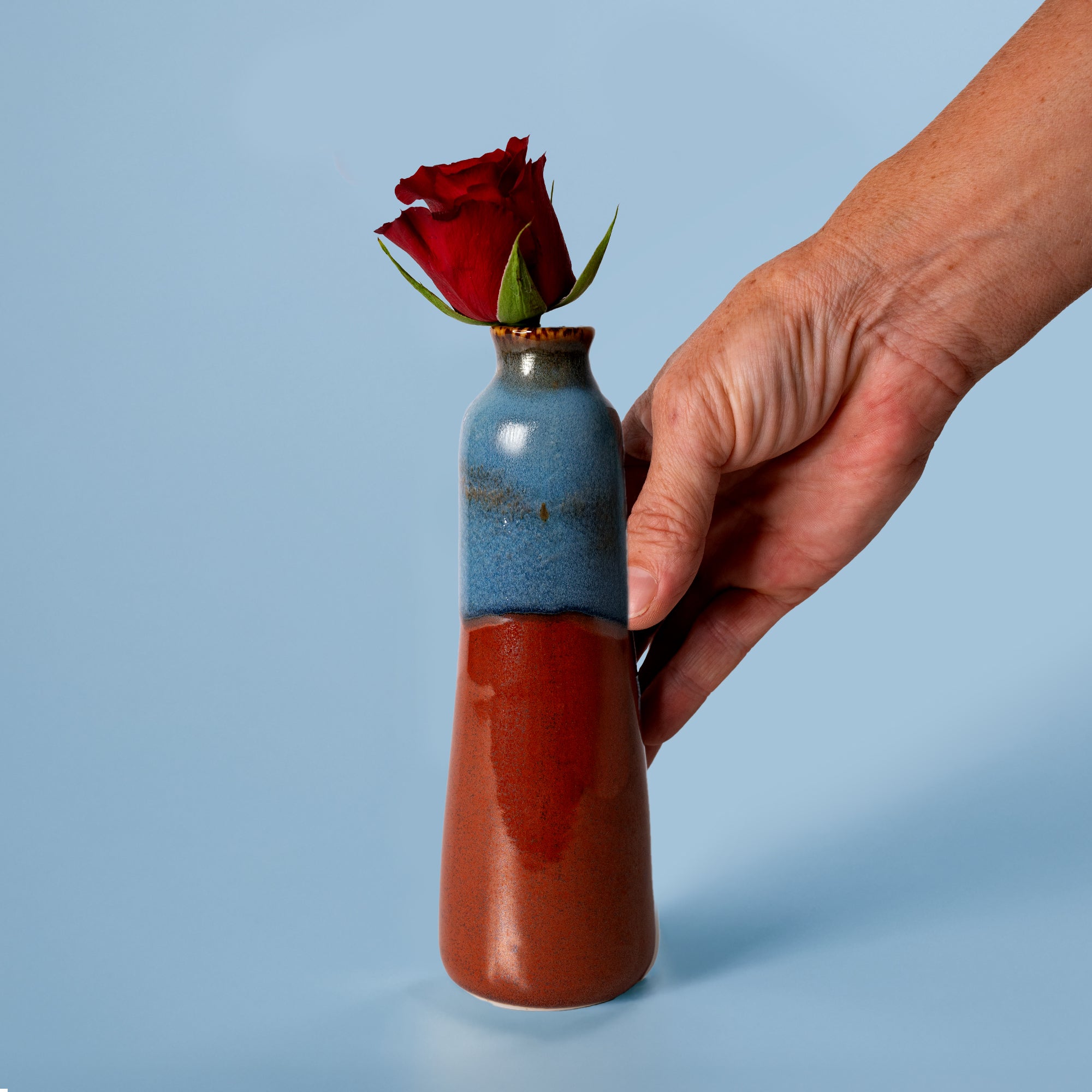 Unique handmade ceramic vase by Pottery For The Planet with blue and brown glaze holding a red rose