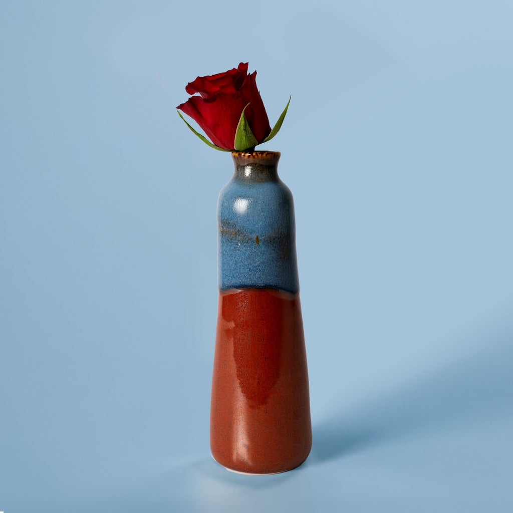 Unique handmade ceramic vase with blue and red glaze holding a single red rose
