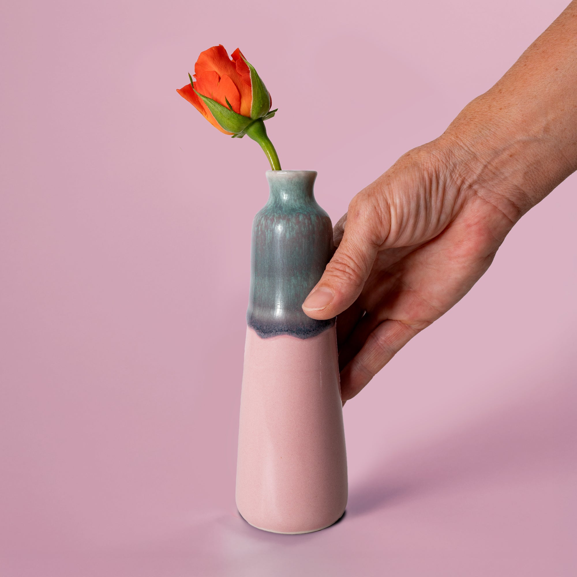 Unique handmade ceramic vase by Pottery For The Planet with soft pink and blue glaze holding a single orange rose