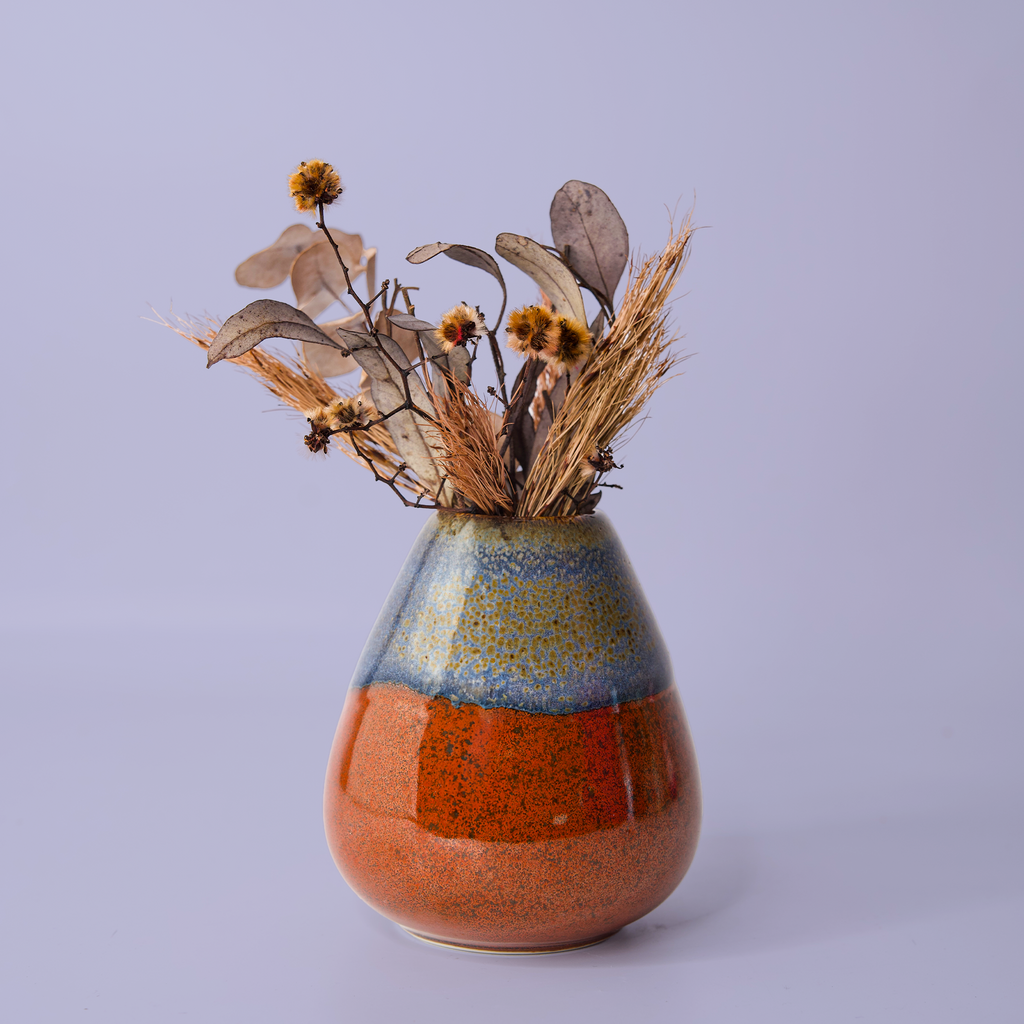 Unique pottery flower vase with blue and orange glaze holding dried flowers and grasses