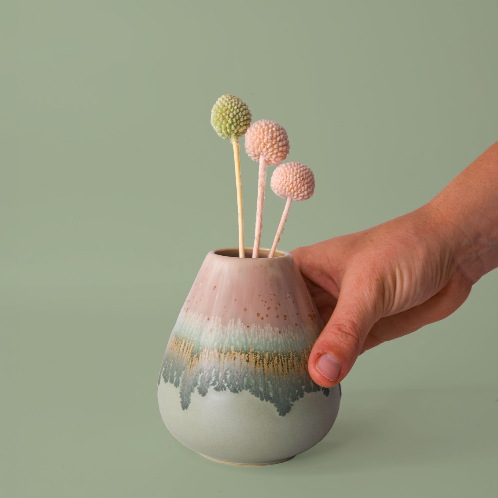 Hand holding a unique pottery flower vase by Pottery For The Planet with pastel colors and decorative textured flowers