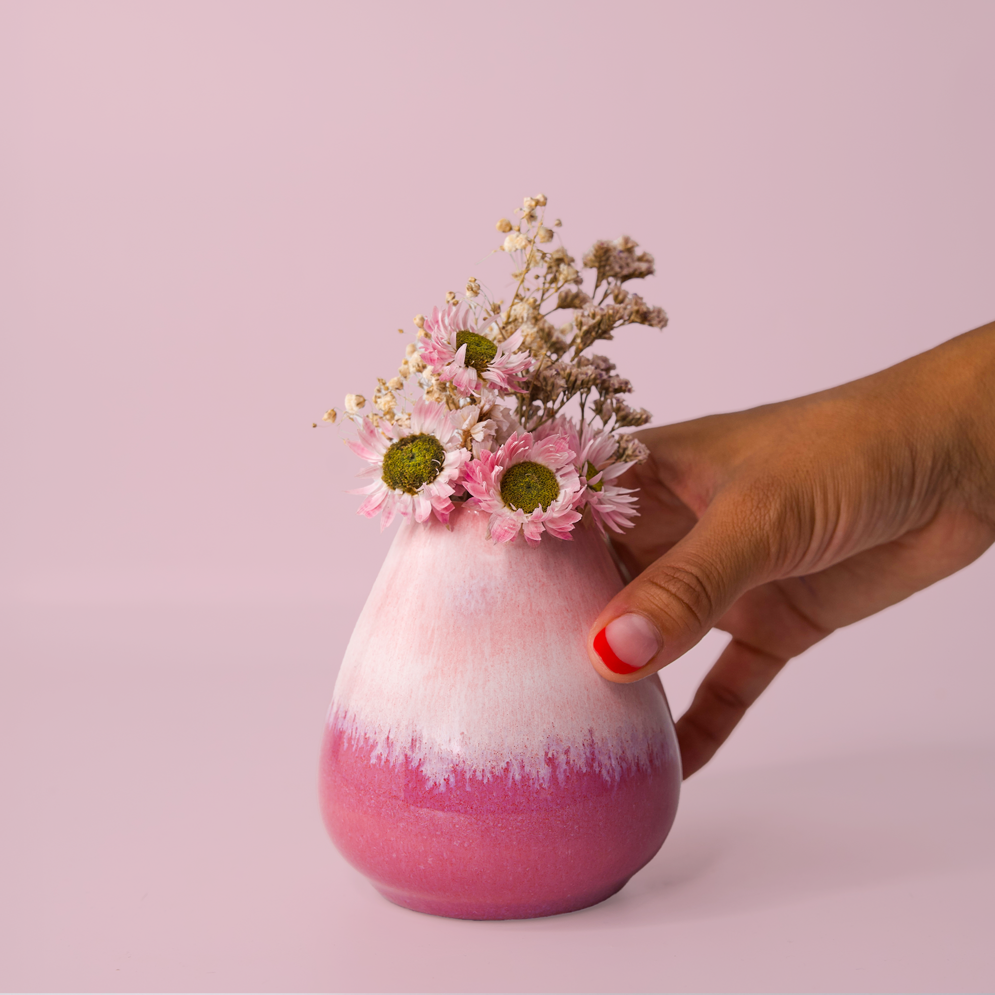 Hand holding unique pottery flower vase with pink and white gradient glaze filled with pink and white flowers
