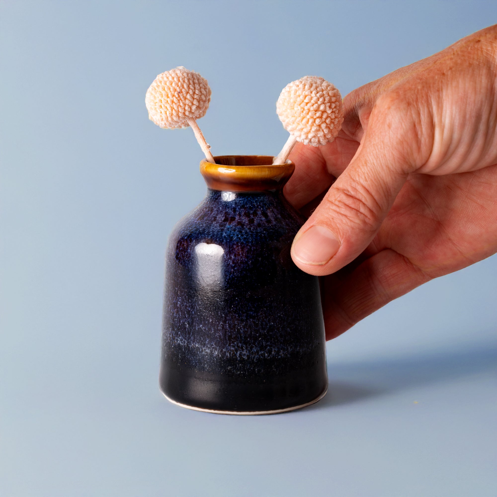 Hand holding a miniature decorative vase for shelf by Pottery For The Planet with two small cream flowers
