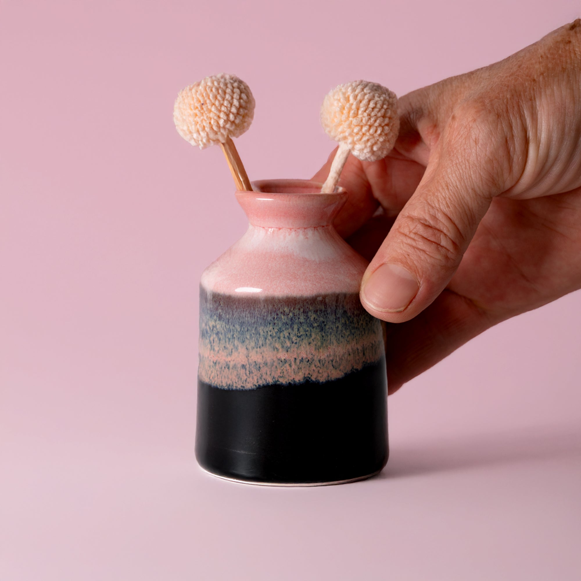 Hand holding a pink black ceramic miniature decorative vase for shelf with dried flower stems
