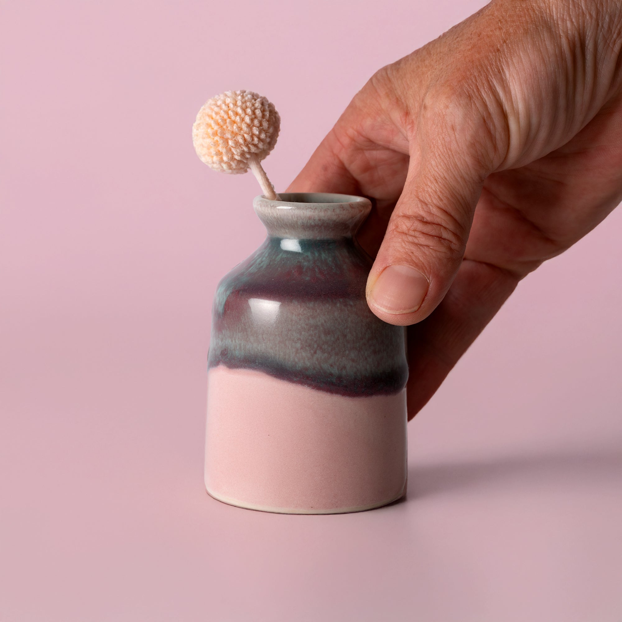 Hand holding a Pottery For The Planet miniature decorative vase for shelf with a small flower inside