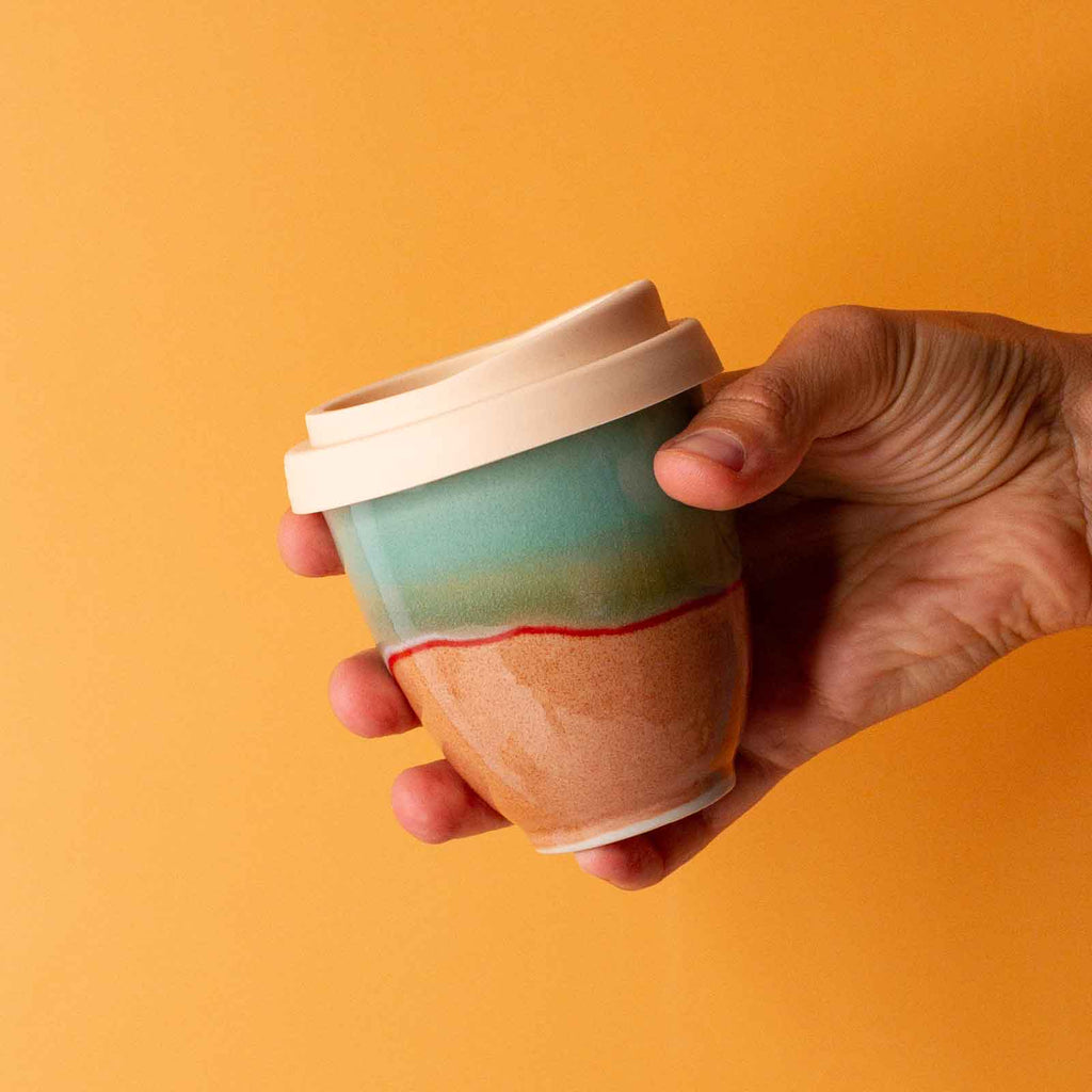 Hand holding colorful handmade reusable cup with silicone lid by Pottery For The Planet
